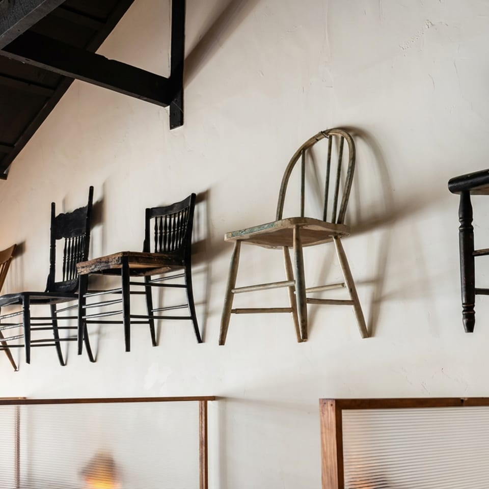 Vintage wooden chairs mounted along a white restaurant wall above frosted glass partitions.