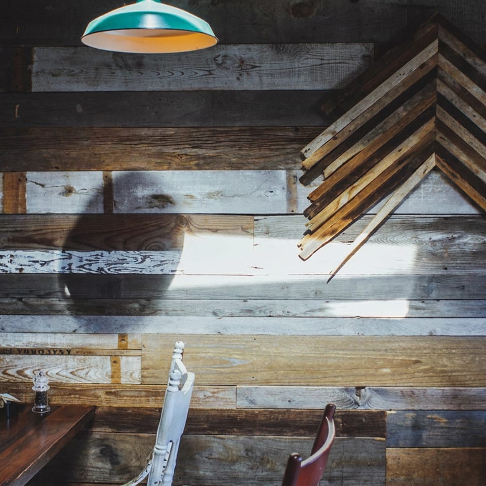 Rustic restaurant interior featuring reclaimed wood walls, a turquoise pendant light, wooden tables, red chairs, and nautical decor.
